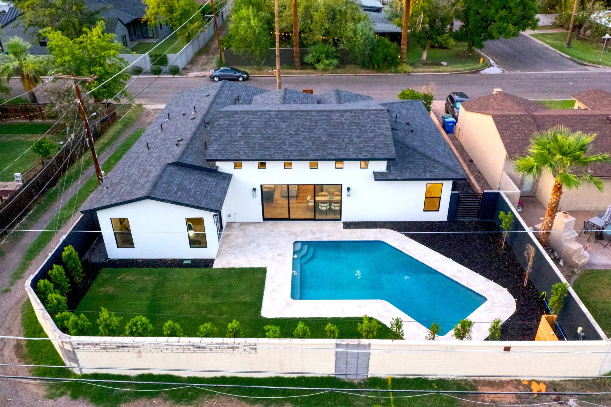 Aerial view of a white modern house with black roof and blue pool at dusk.