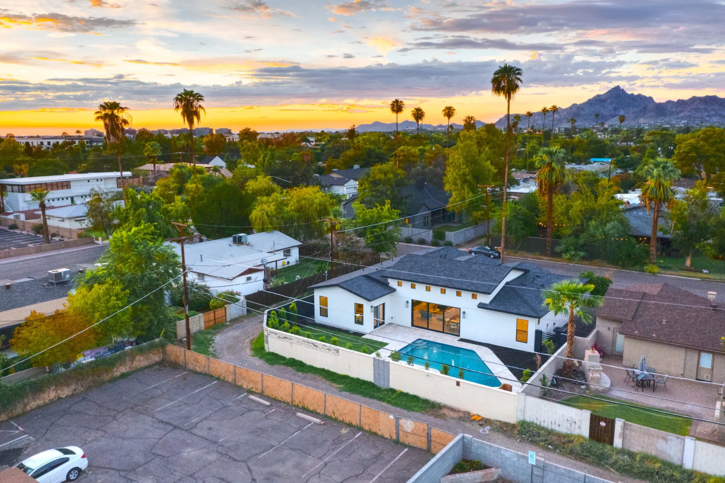 Aerial view of a modern white house with pool beneath a vivid orange sunset sky.