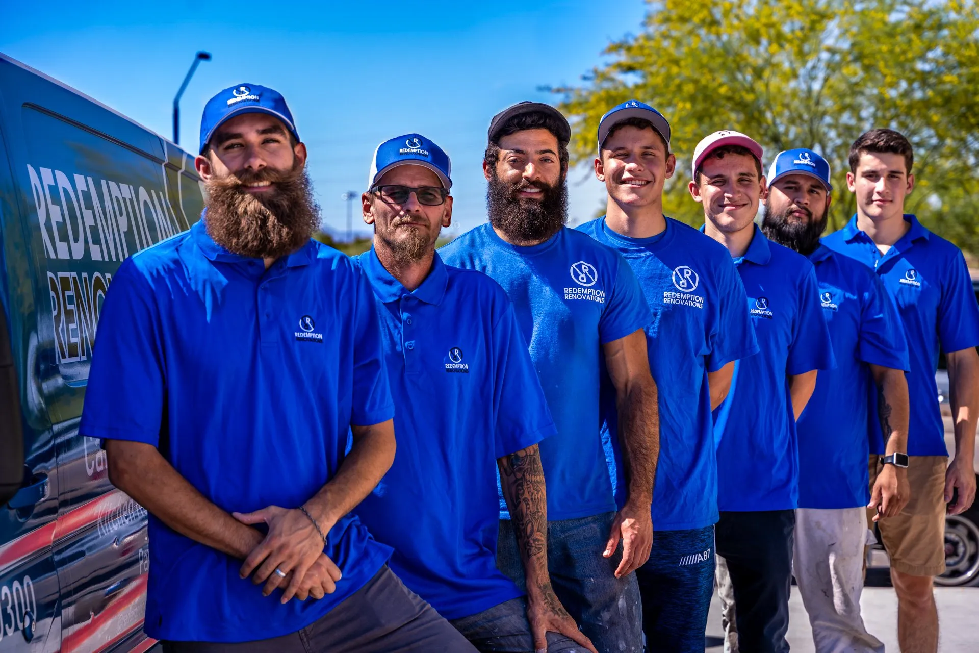 Group of men in matching blue polo shirts lean together and smile for the camera.