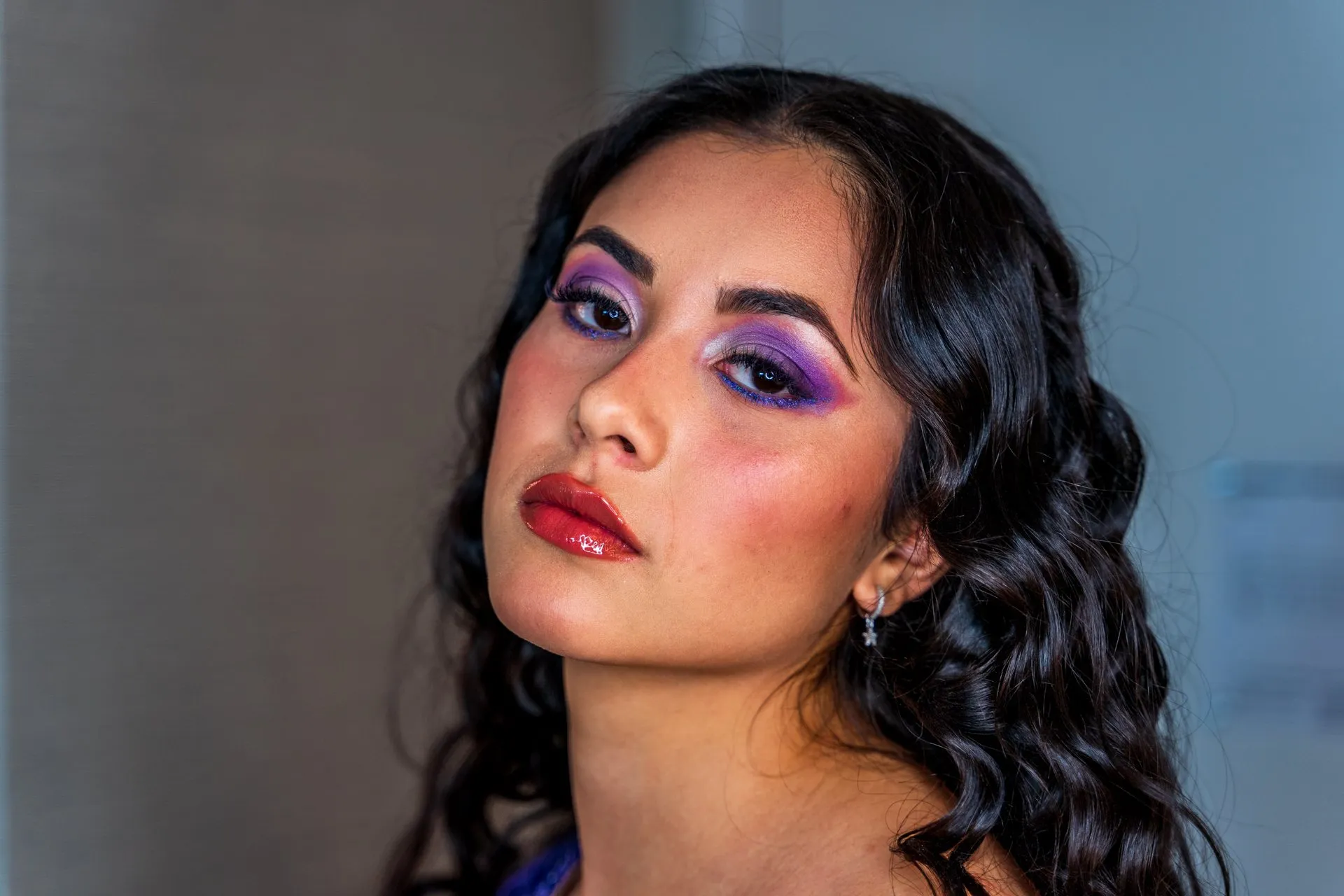 Close portrait of a young woman with dramatic purple eye makeup and dark curly hair.