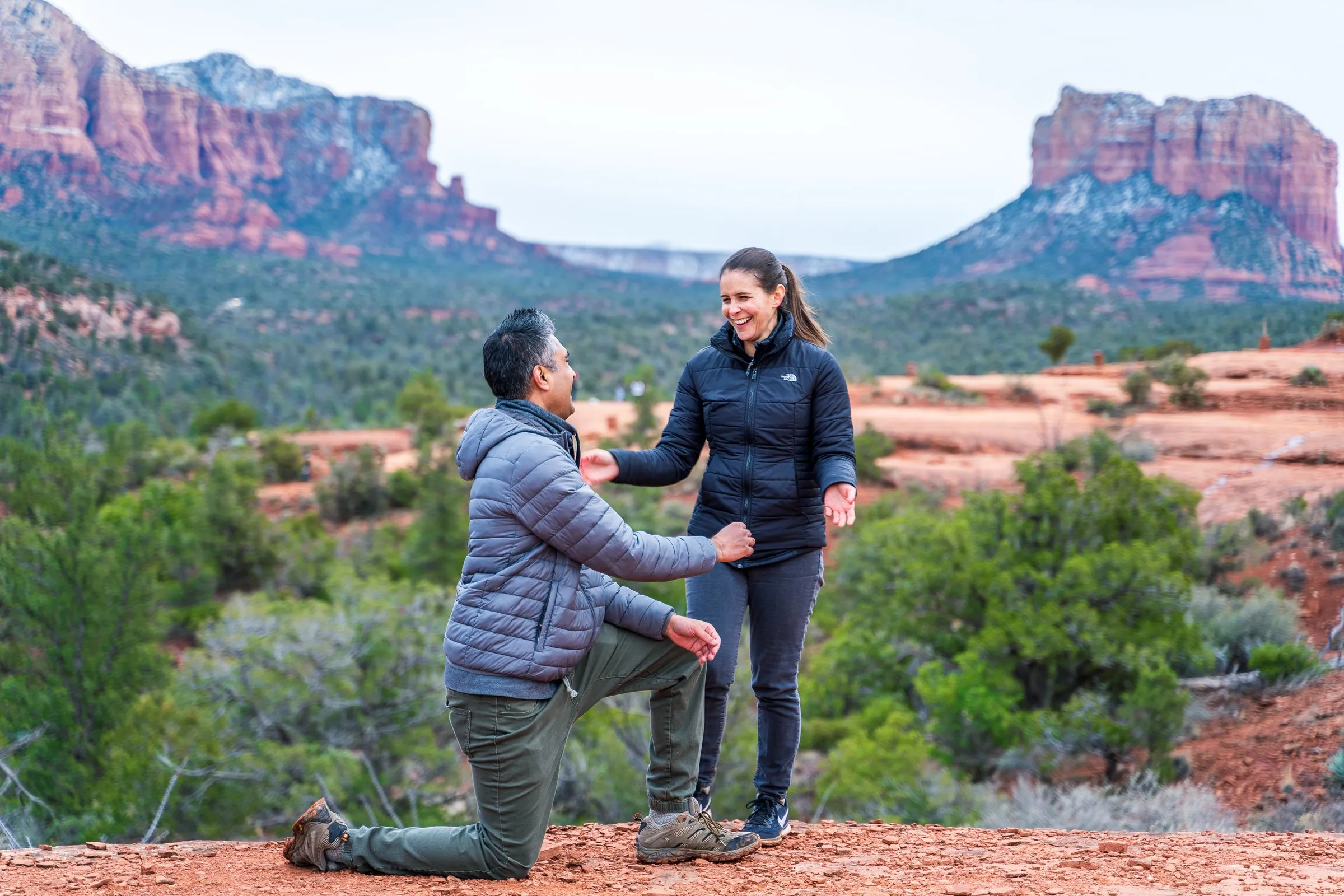 Man kneels before a woman on a desert overlook with red rock buttes behind.