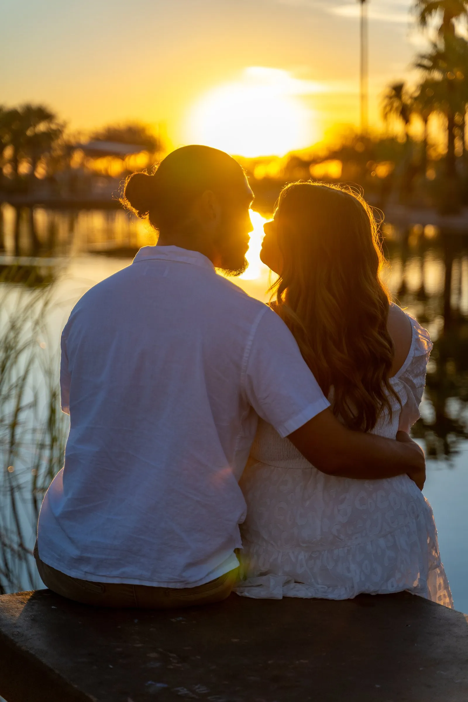 Couple about to kiss in silhouette as the sun sets over a lake.
