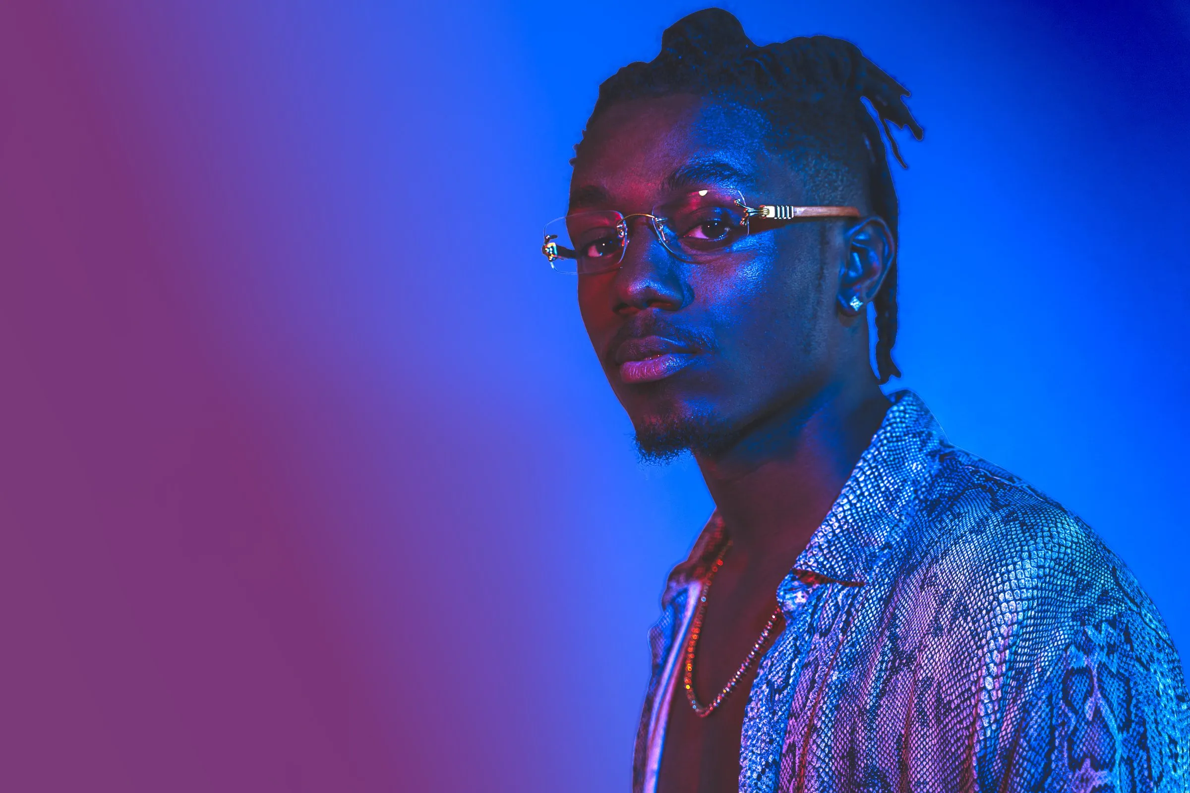 Man with glasses and a patterned shirt lit by vivid blue and magenta light.