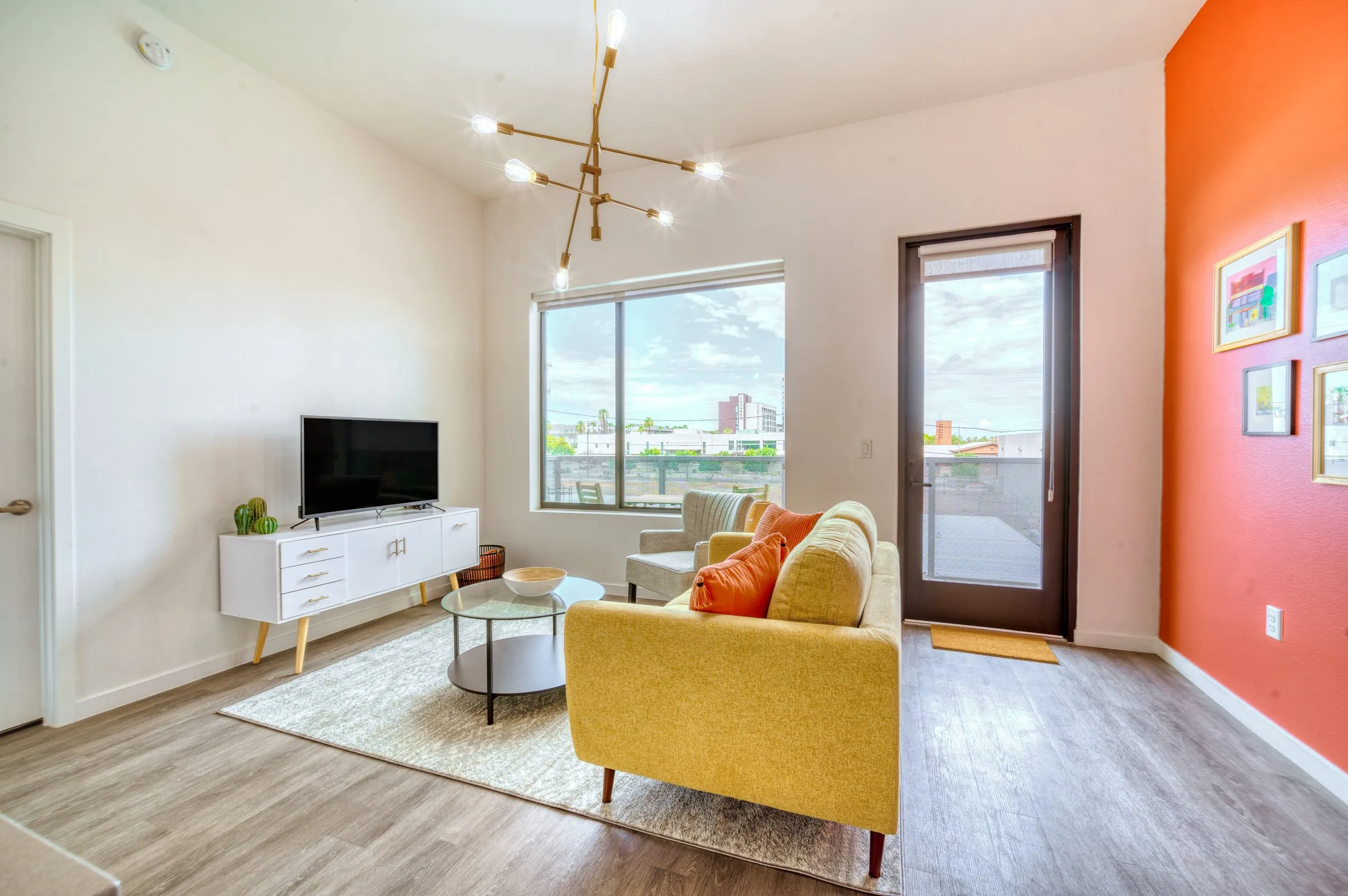 Bright living room with yellow sofa, orange accent wall, gold chandelier and balcony door.