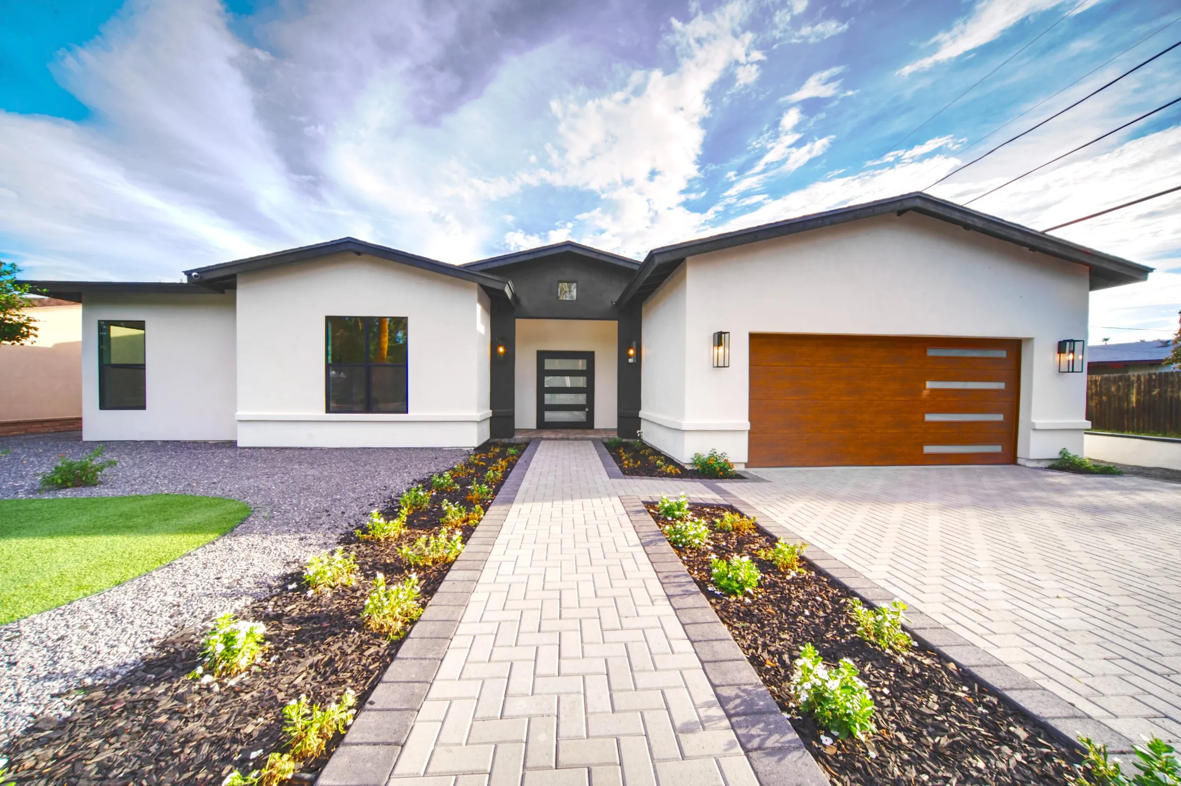 Modern single-story white home with a brick paver walkway under a dramatic cloudy sky.