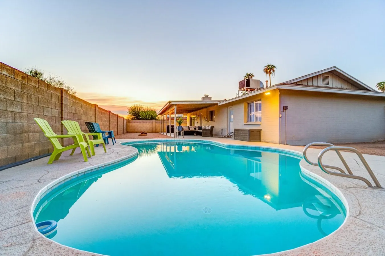 Backyard swimming pool at dusk with green lounge chairs and a softly lit house beyond.
