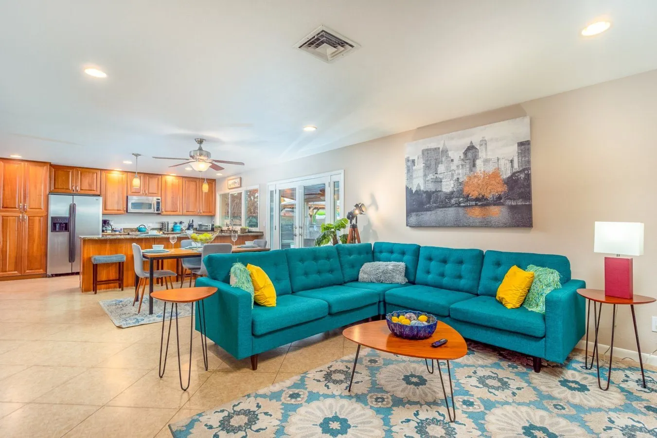Bright open living room with a teal sectional sofa and a kitchen beyond.