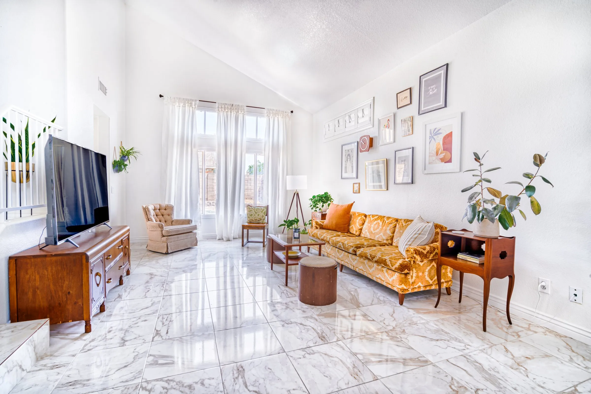 Bright living room with a marble floor, mustard sofa, gallery wall and tall windows.